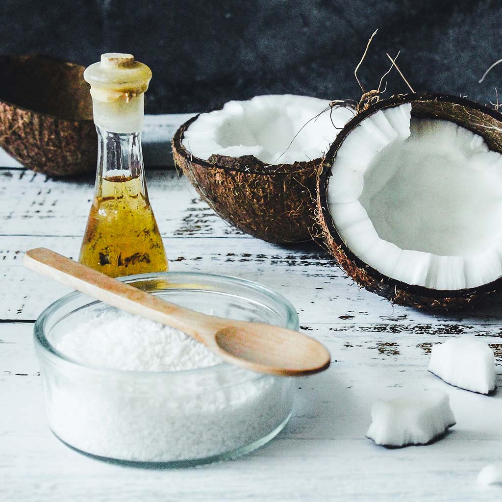 Coconut oil, kernel and open shells pictured on a rustic table. Photo by Tijana Drndarski.