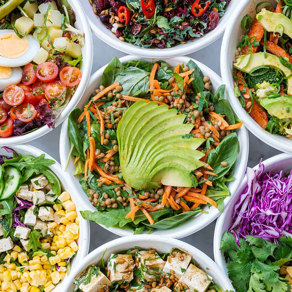 Multiple salad bowls with many fresh healthy ingredients including avocado, pumpkin seeds, spinach and others. Photo by Luisa Brimble.