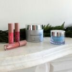 Rodan + Fields Plumping Lip Oil, Active Hydration Body Replenish, and Hydra Mask Gel Cream pictured on a marble shelf with holiday garland.